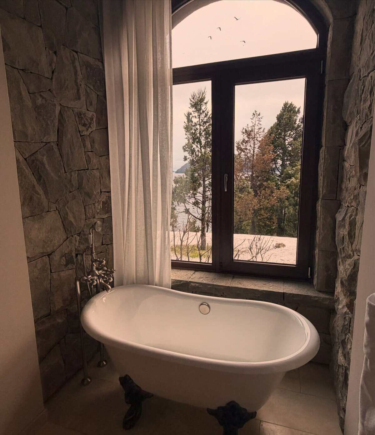 Baño con bañera blanca y ventana que da a un paisaje natural en Bariloche
