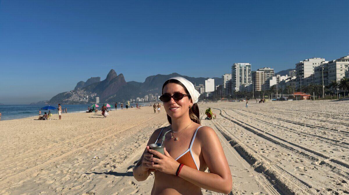 Leticia Siciliani en la playa de Río de Janeiro, sosteniendo un vaso y sonriendo