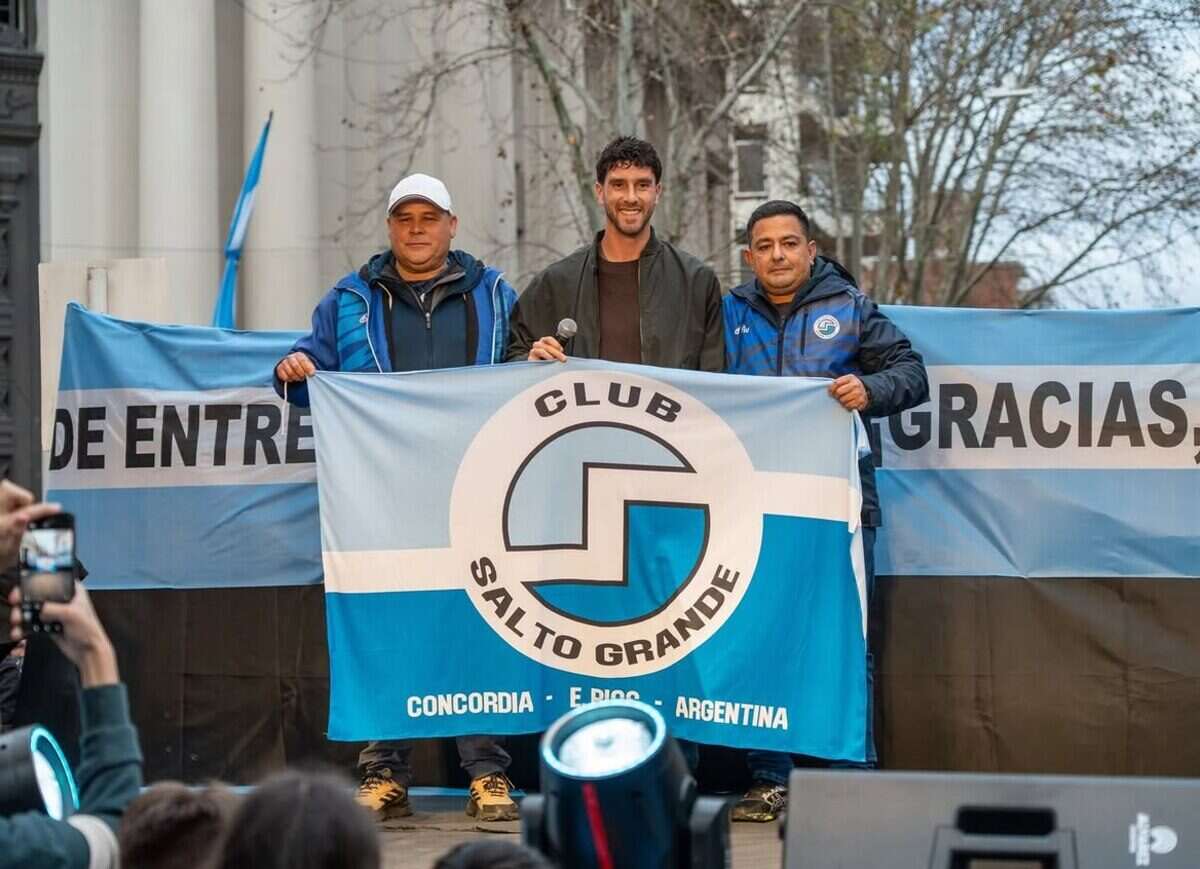 Tres hombres sosteniendo una bandera del Club Salto Grande en un evento público