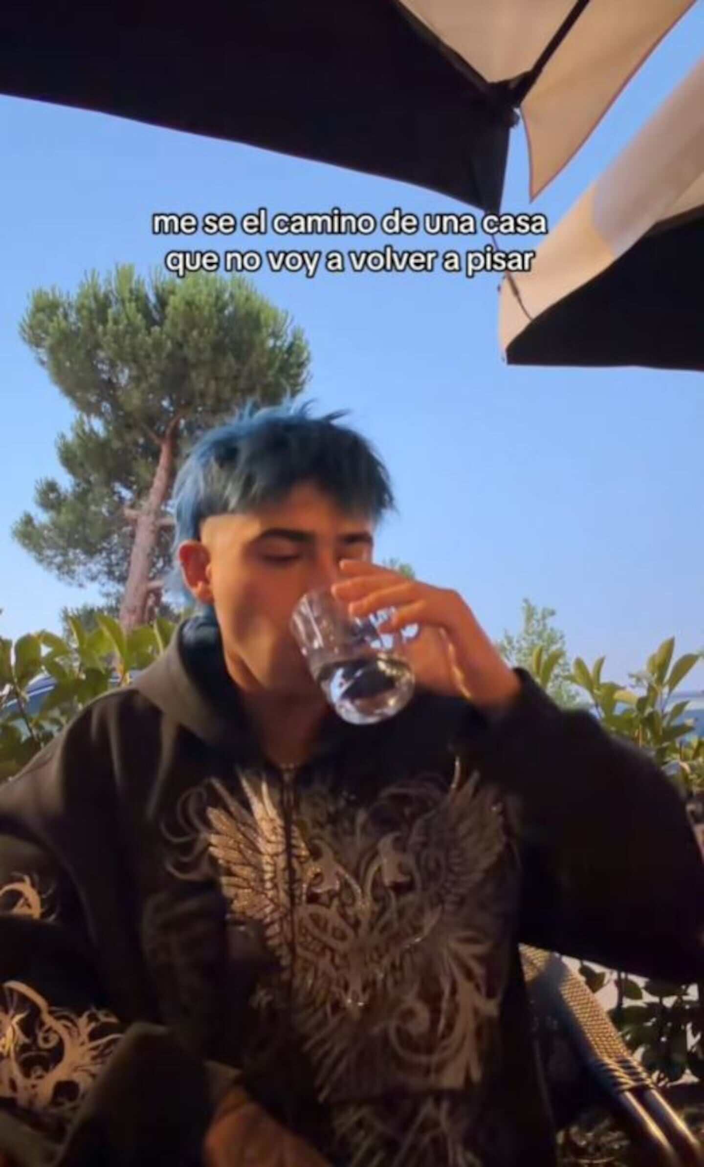 Luck Ra sentado en una terraza con un vaso en la mano, mirando hacia el frente