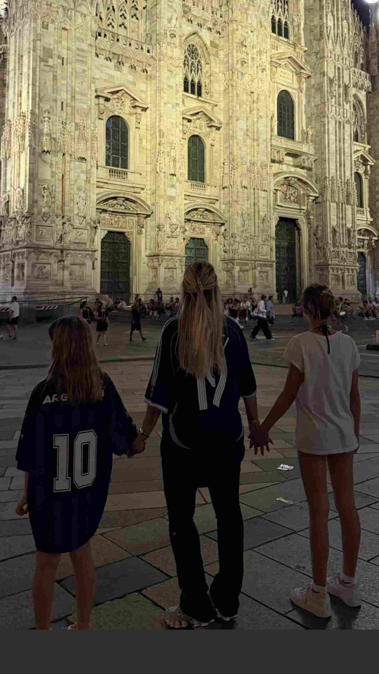 Mujer y dos niñas de espaldas en una plaza, frente a una catedral iluminada