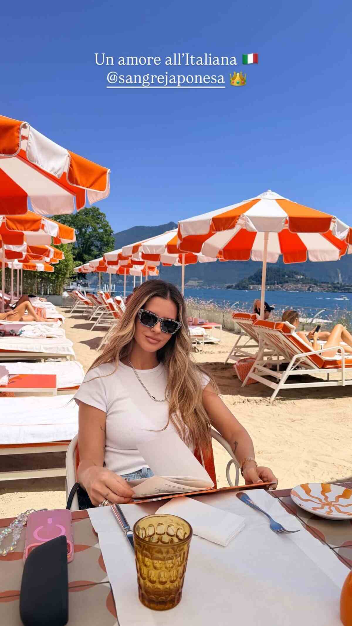 Mujer sentada en una playa con sombrillas naranjas y blancas, sosteniendo un menú