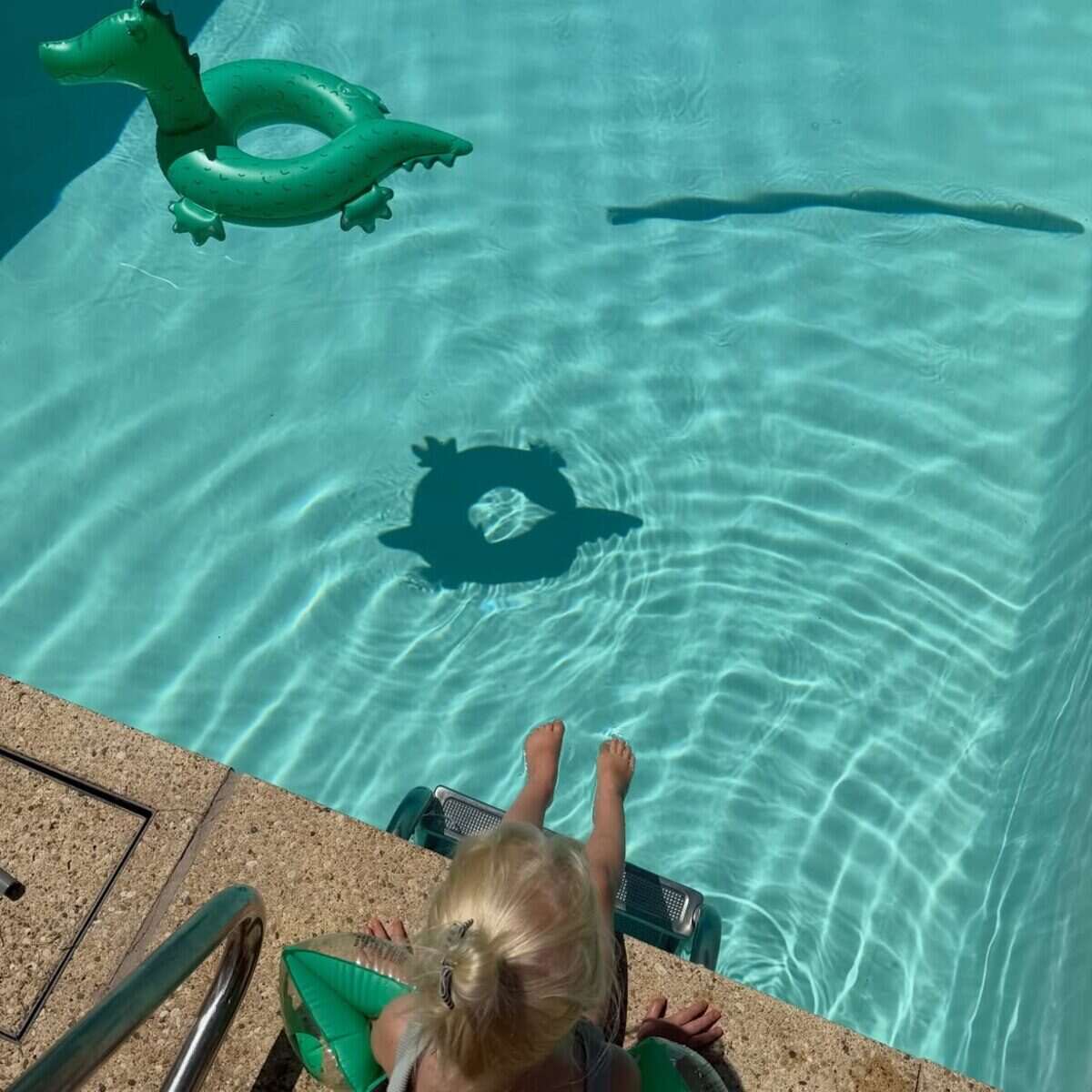 Niña pequeña sentada al borde de una piscina con flotador en forma de dragón