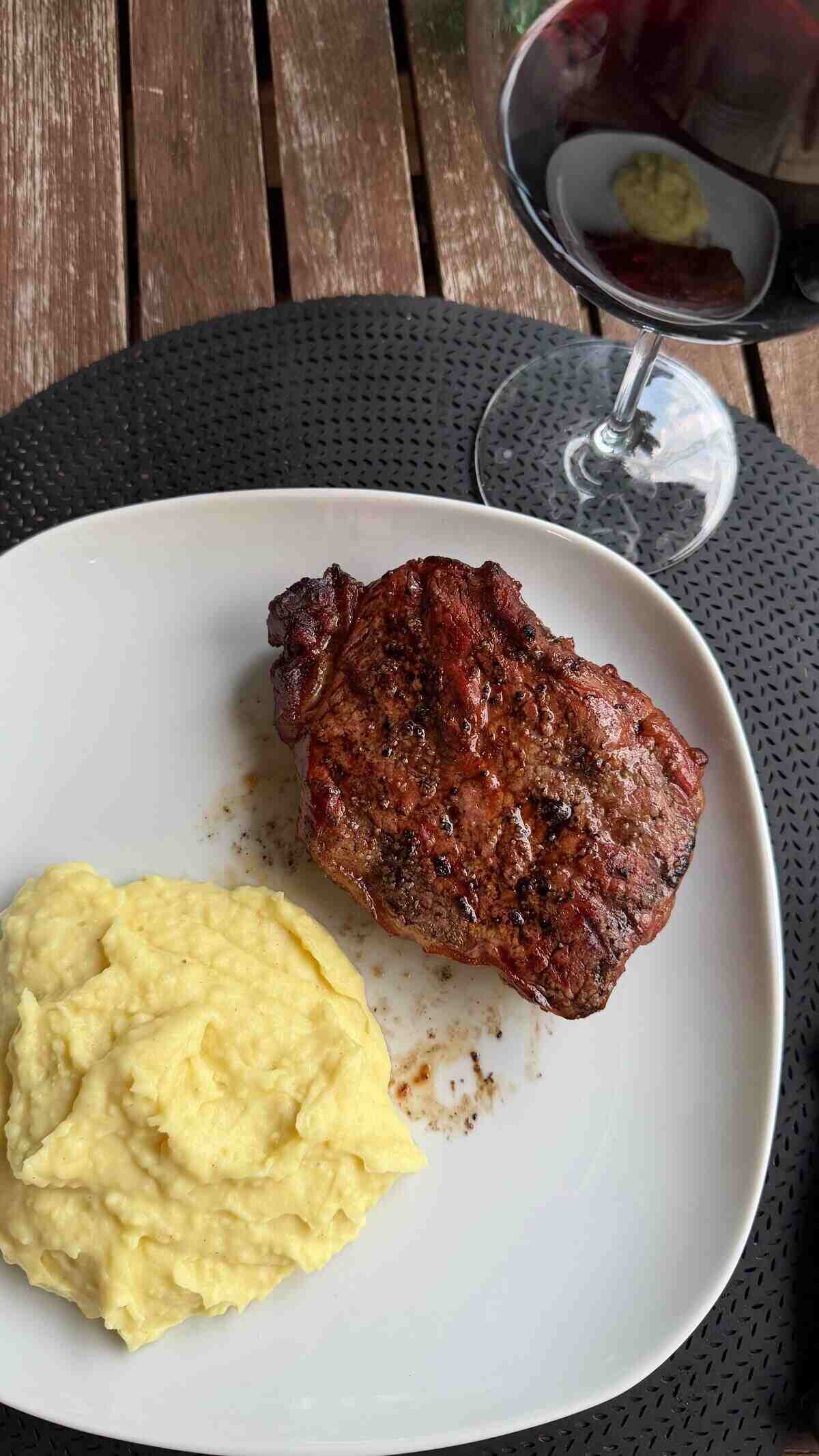 Plato de carne asada con puré de patatas y una copa de vino tinto