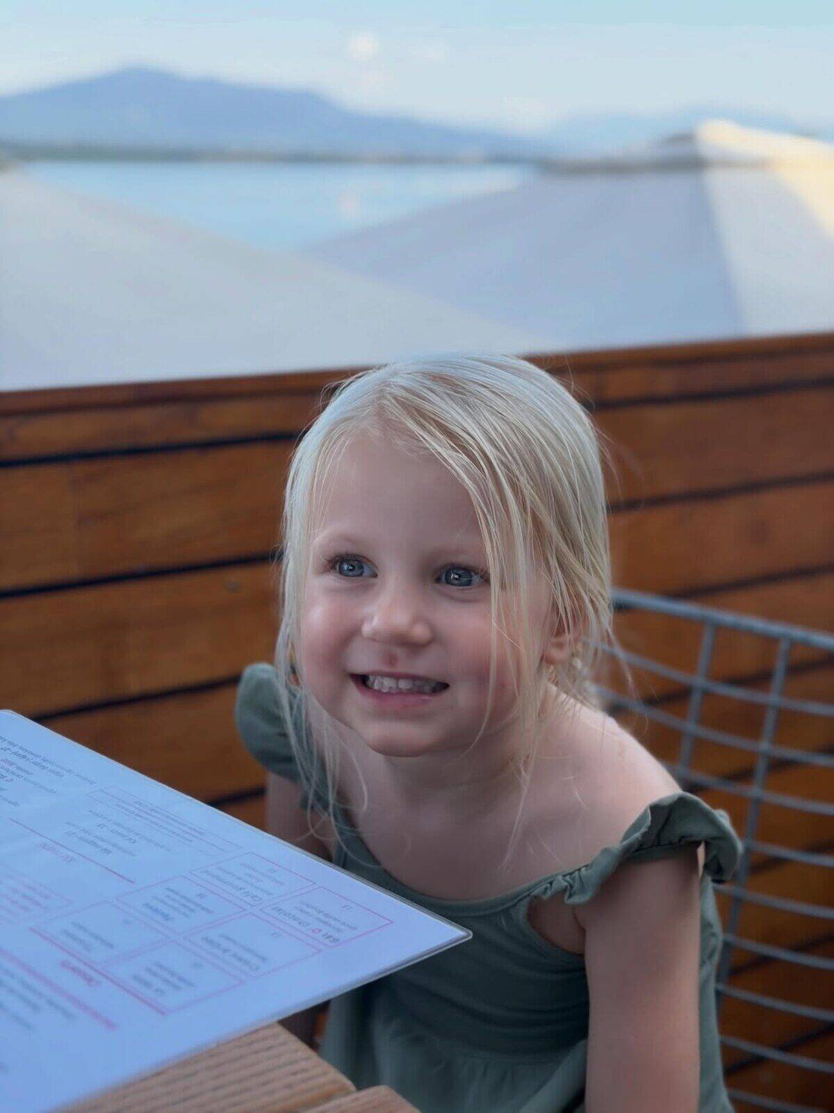 Niña sonriente con cabello rubio en un restaurante al aire libre en Suiza