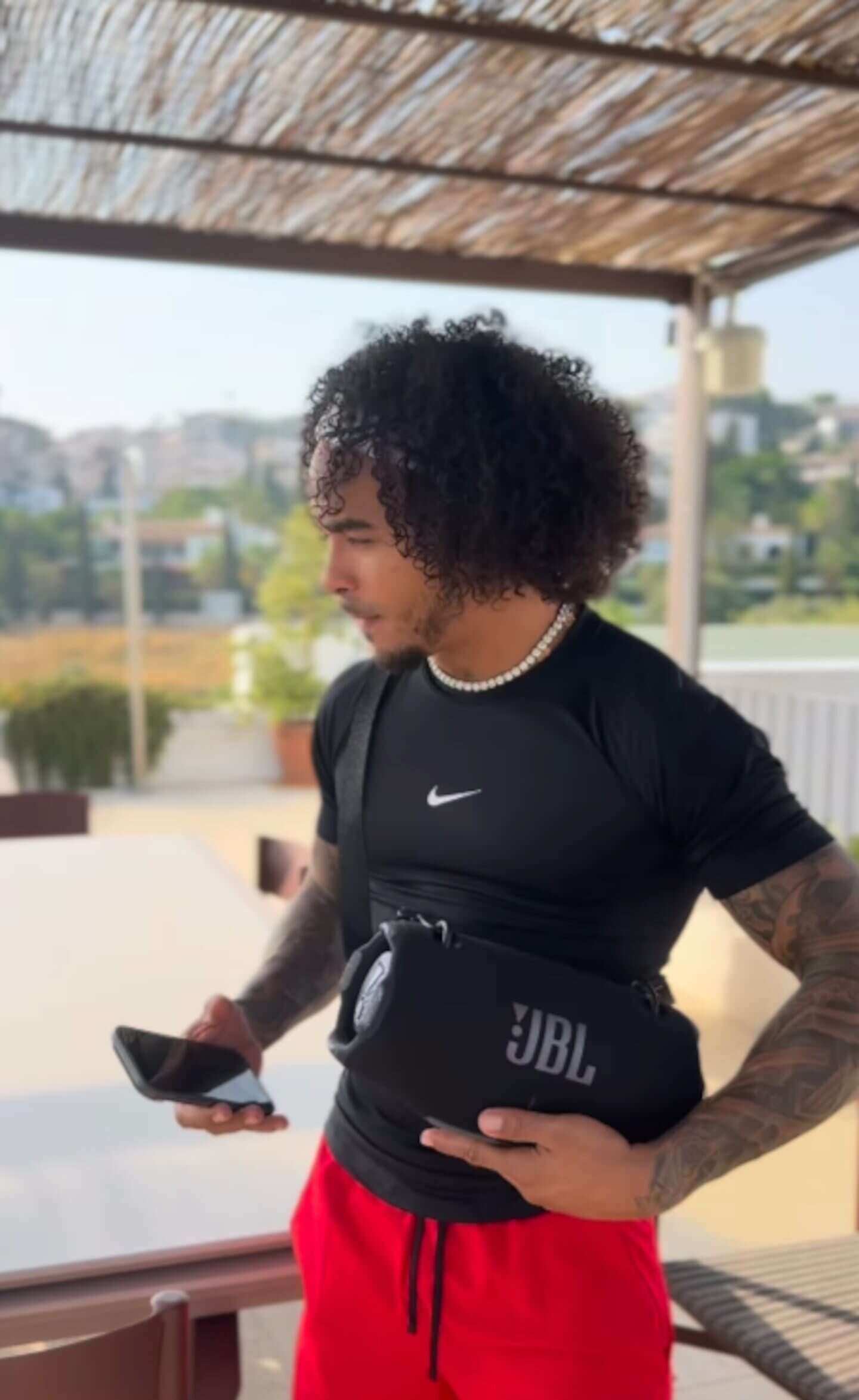Ozuna con un teléfono móvil en la mano, vestido con camiseta negra y pantalones rojos