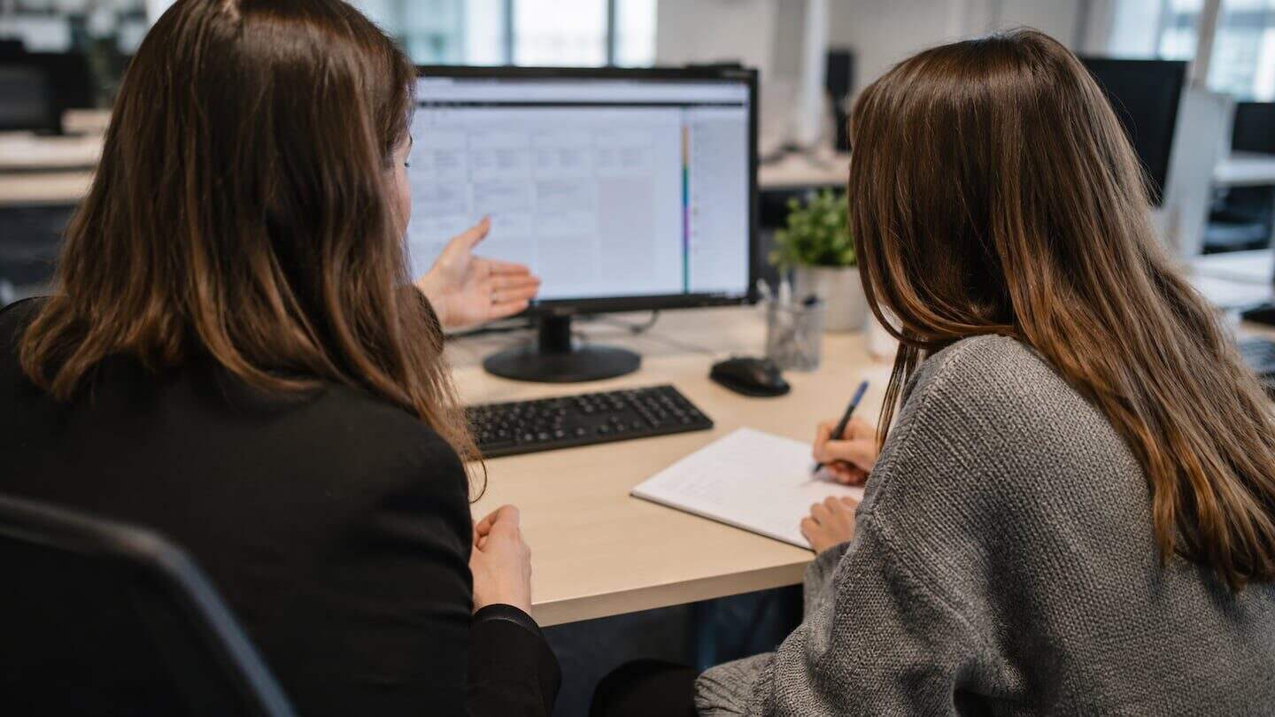 Dos mujeres conversando frente a una computadora en un entorno de trabajo