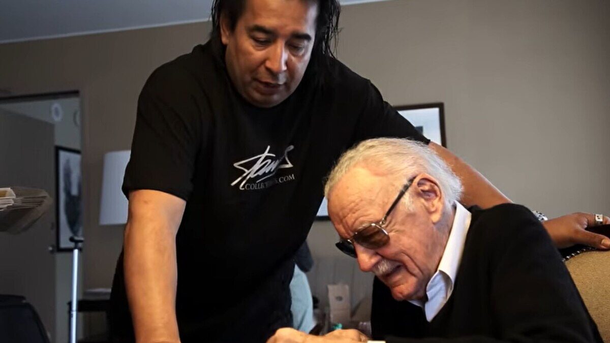 Stan Lee firmando autógrafos con un hombre de pie a su lado