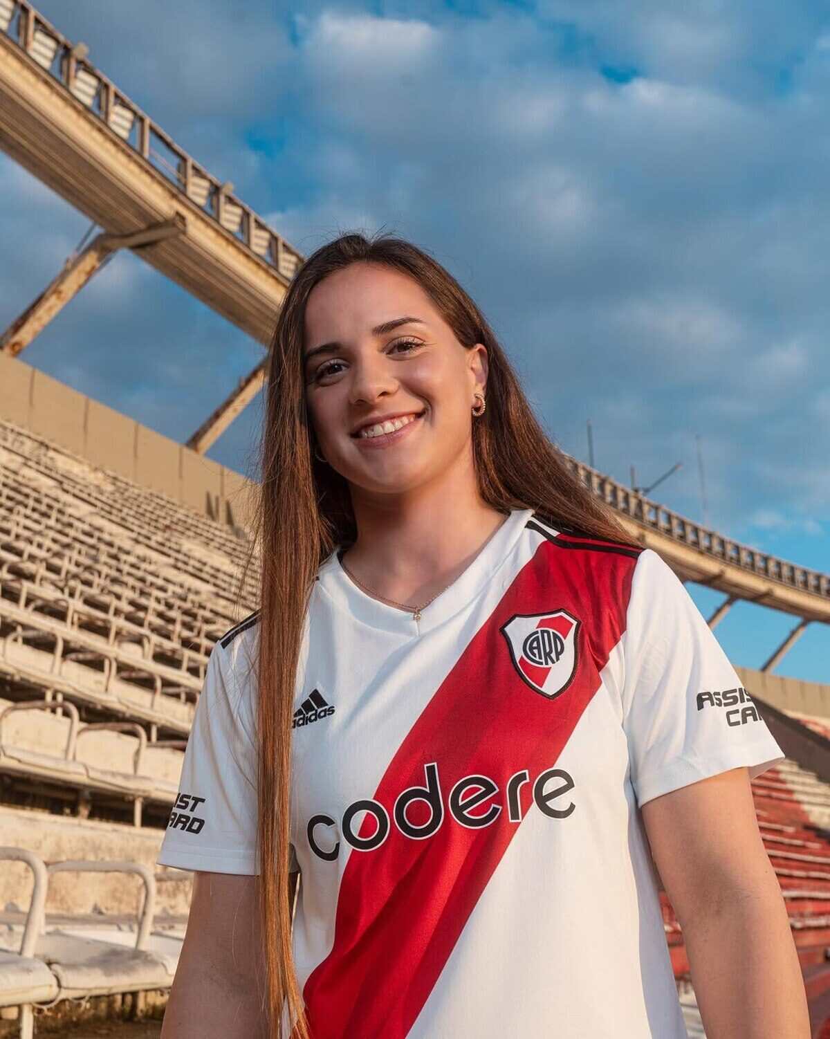 Jugadora de Racing Club sonriente con camiseta del equipo en un estadio vacío