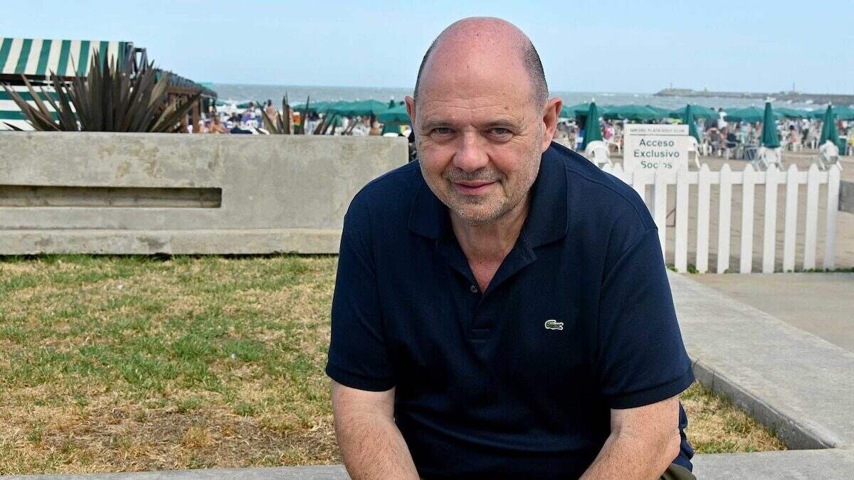 Hombre sentado en un entorno al aire libre, con fondo de playa y sombrillas