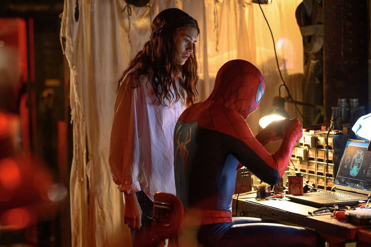 Spider-Man trabajando en su equipo mientras Zendaya lo observa en un taller