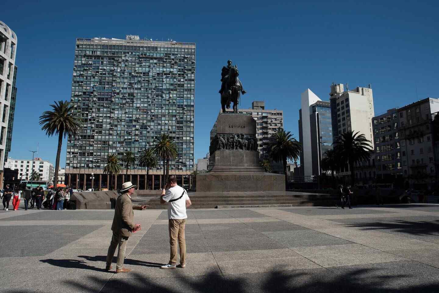 Dos hombres conversan frente a una estatua en una plaza de Montevideo, Uruguay