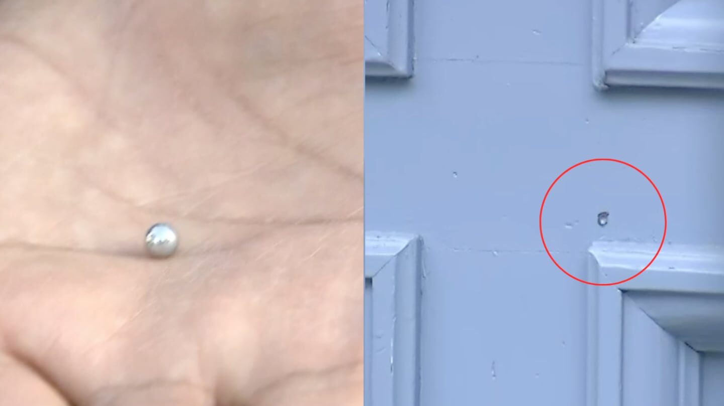Balín en la mano junto a un agujero de bala en una puerta