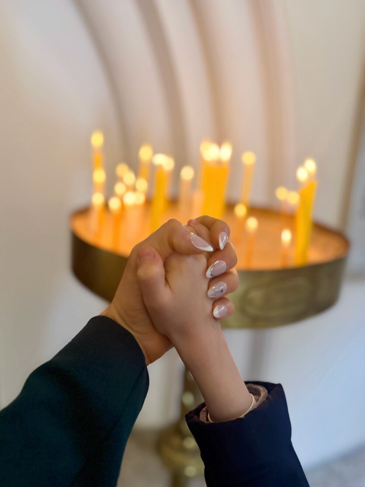 Manos entrelazadas de Vicky Xipolitakis y su hijo Salvador frente a velas encendidas