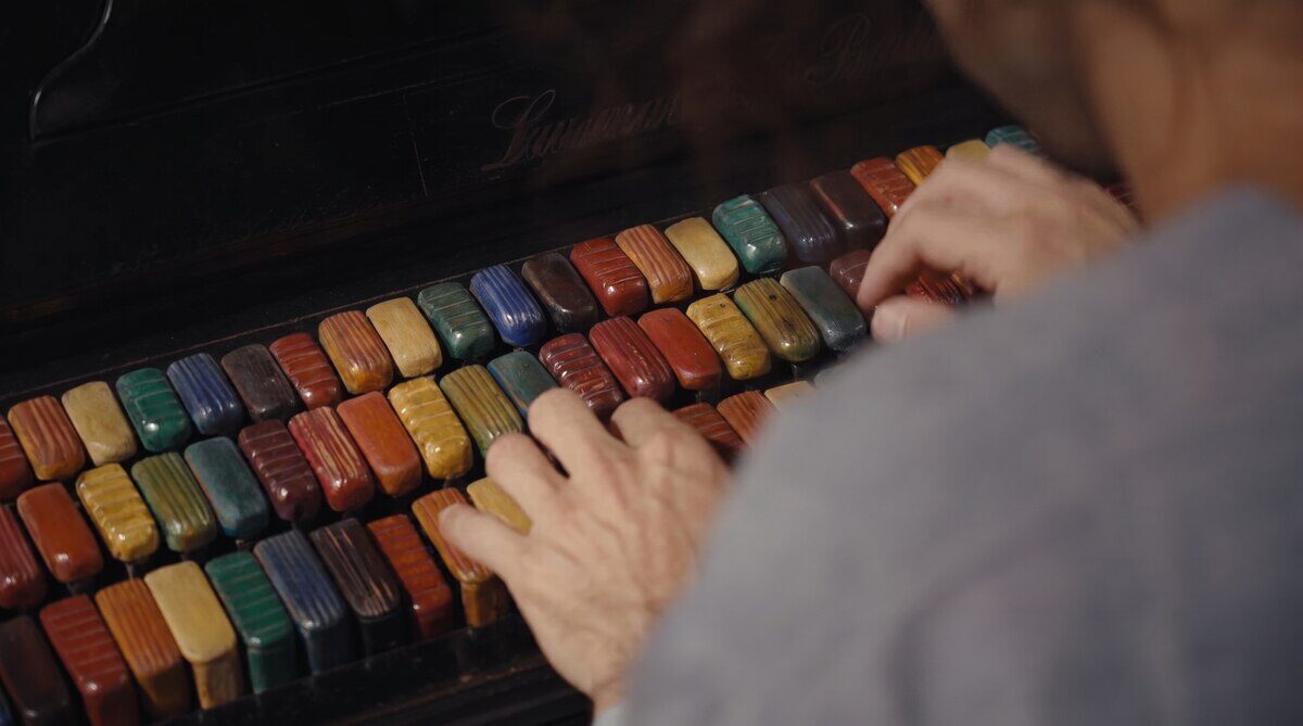 Manos tocando un piano intervenido por Xul Solar con teclas de colores