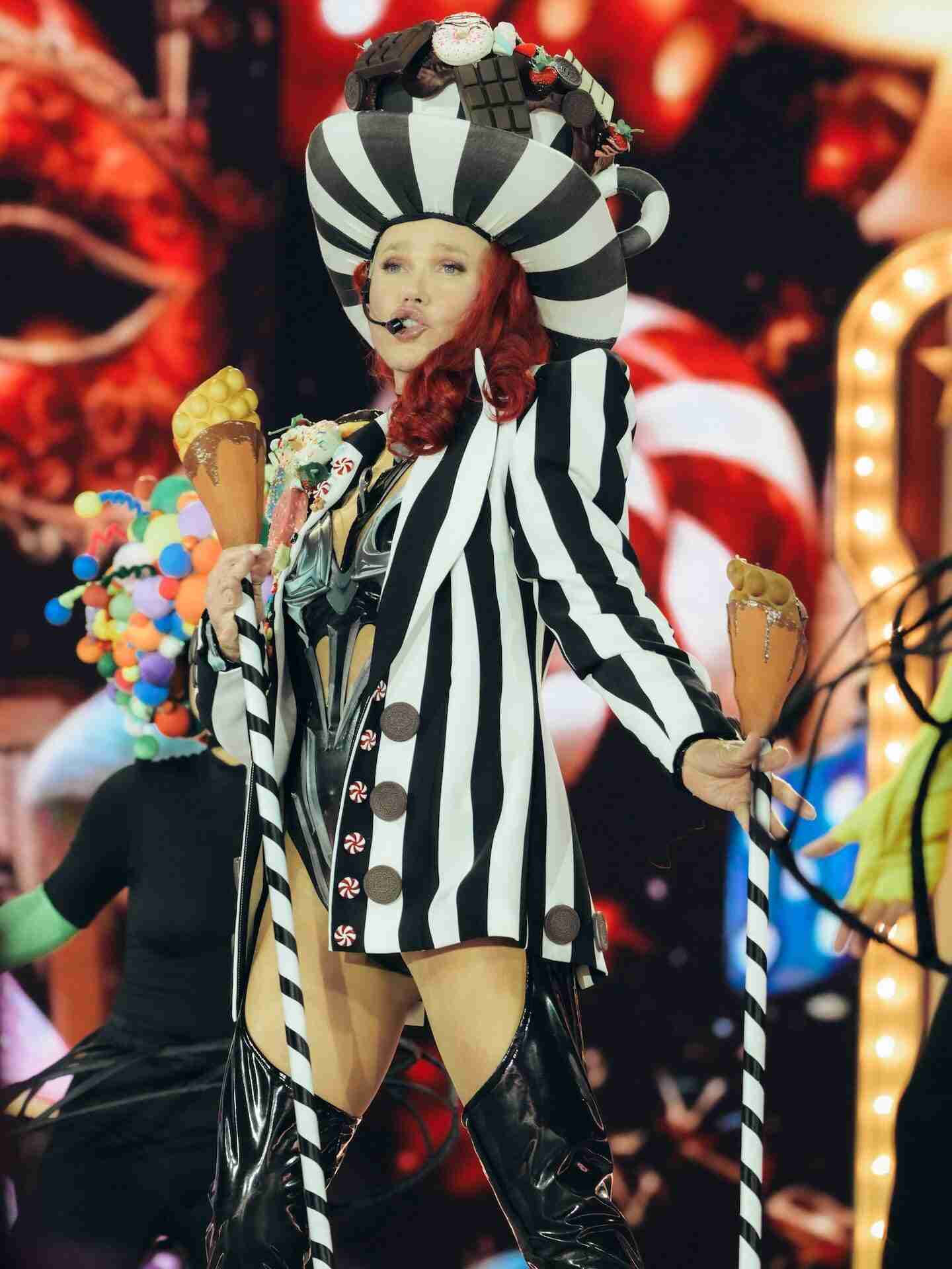 Xuxa Meneghel en su gira de despedida, luciendo un atuendo llamativo con rayas y un sombrero extravagante