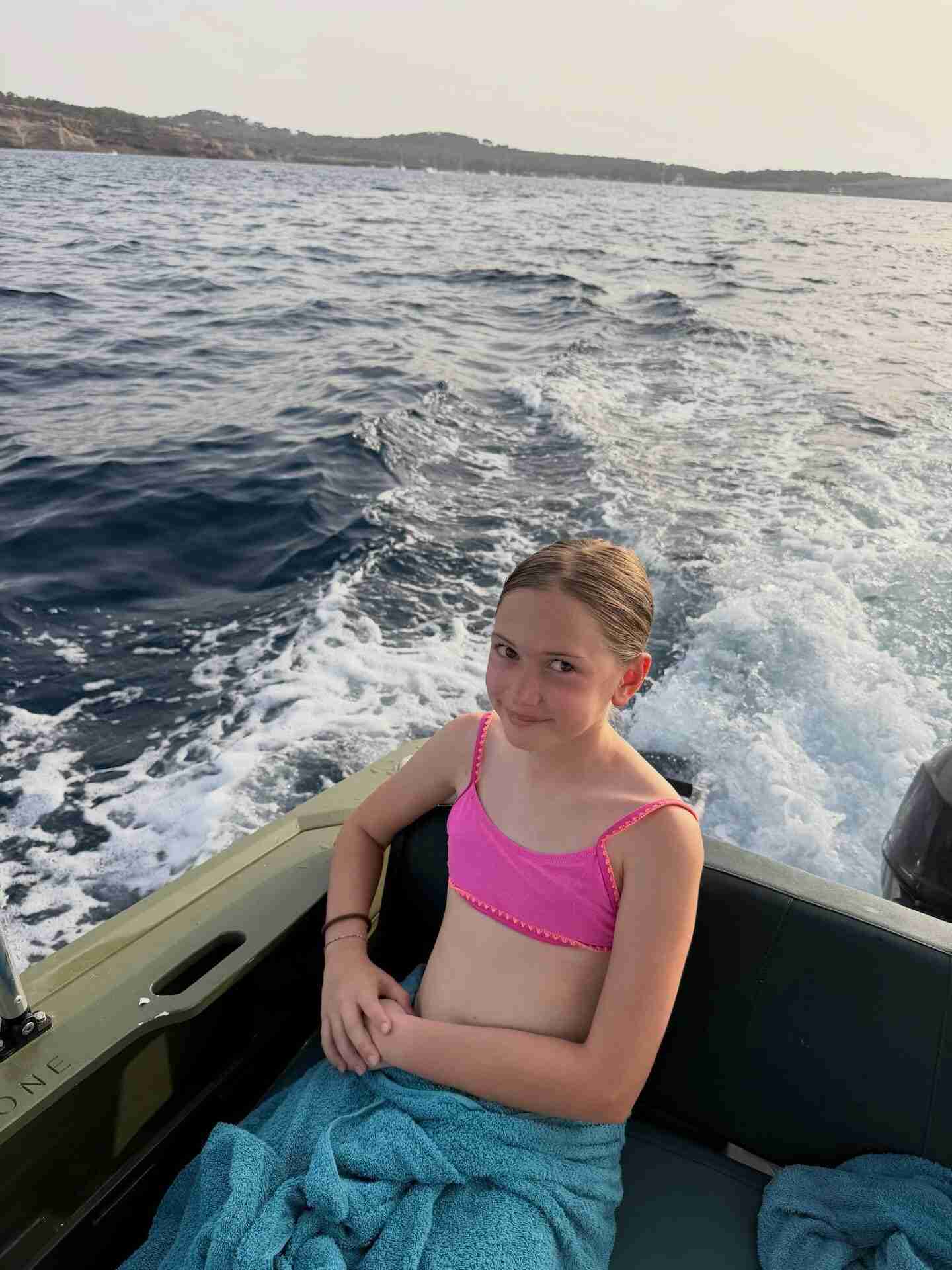 Niña en un bote en Ibiza con un traje de baño rosa y toalla azul