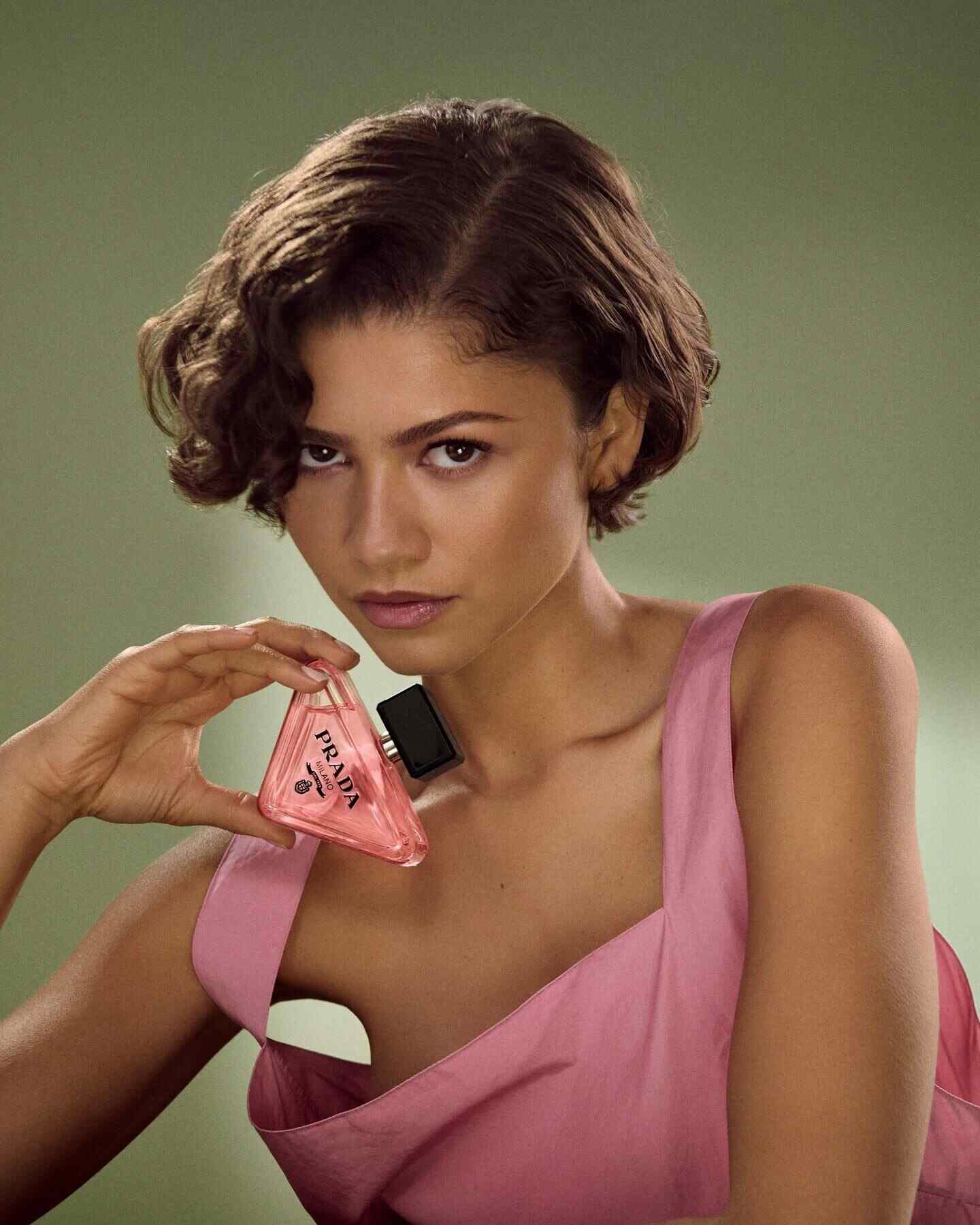 Zendaya posando con un frasco de perfume de Prada en un vestido rosa